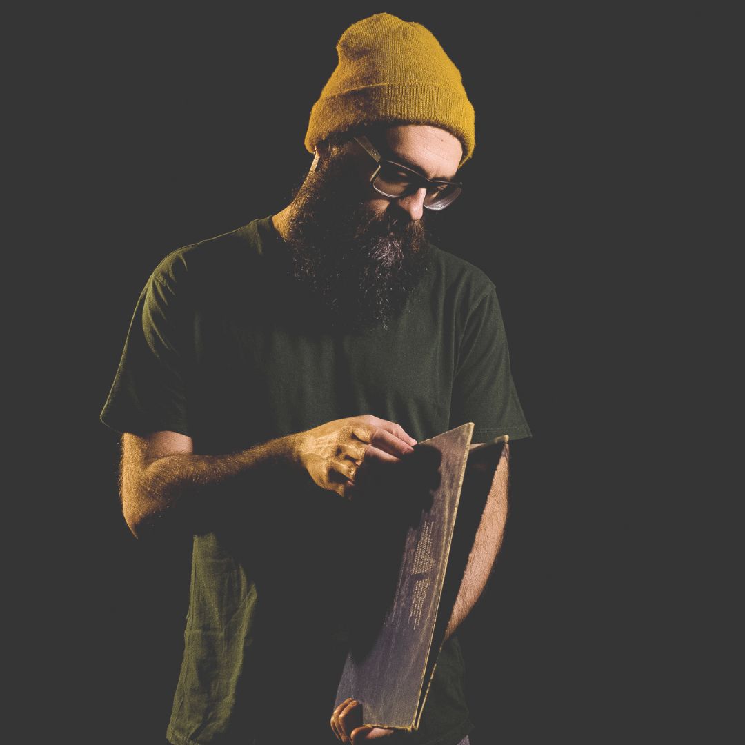 G Nicastro standing bearded man with yellow beanie holding a gatefold record against black background