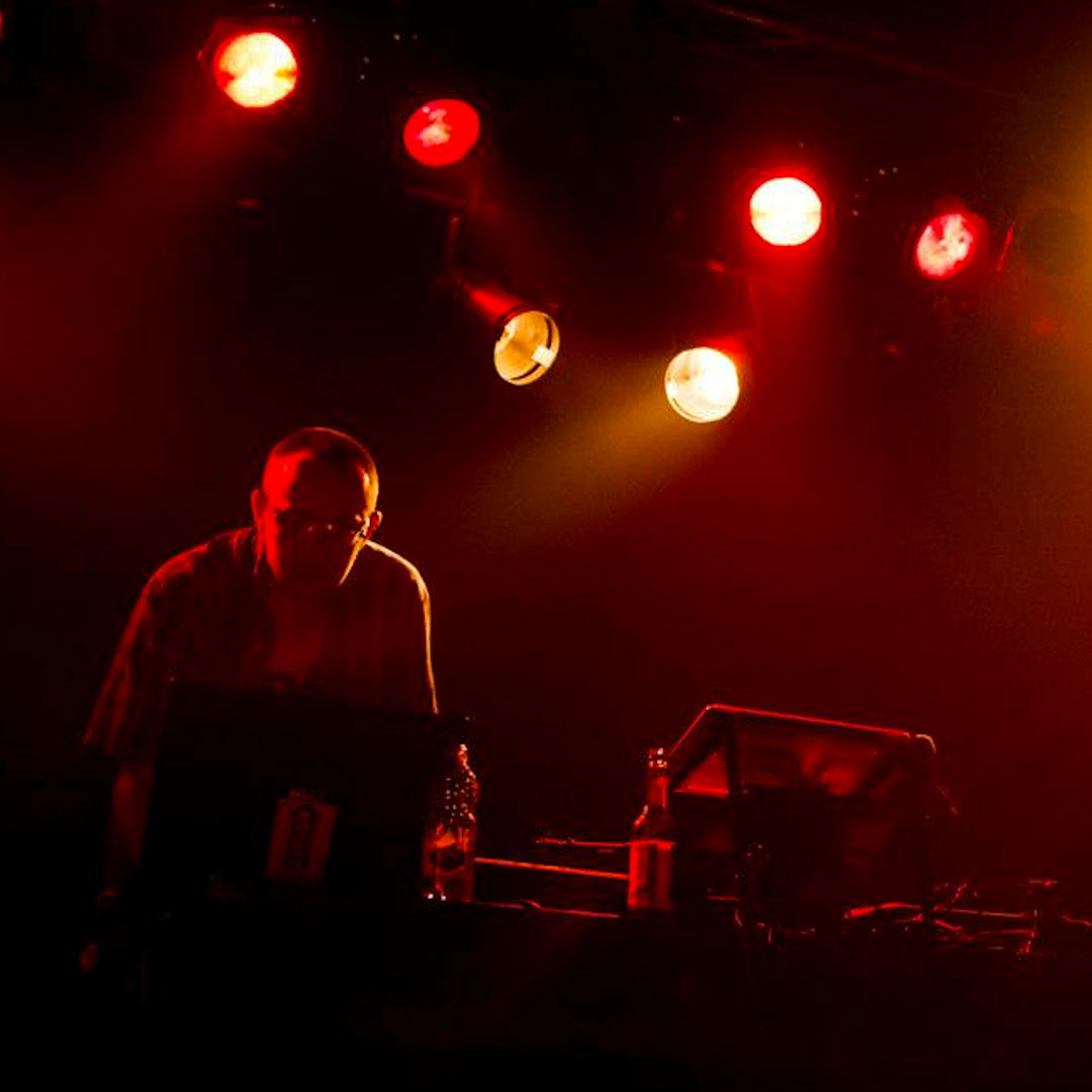 Erma from Casa Degli Specchi on stage playing turntables, black background and red spotlights