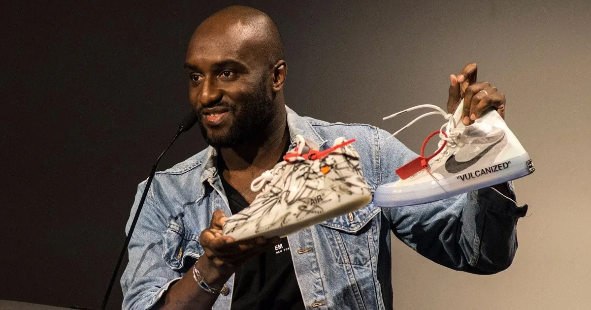 A black man designer named Virgil Abloh holding two of his sneakers collaborations between Nike and Off-White
