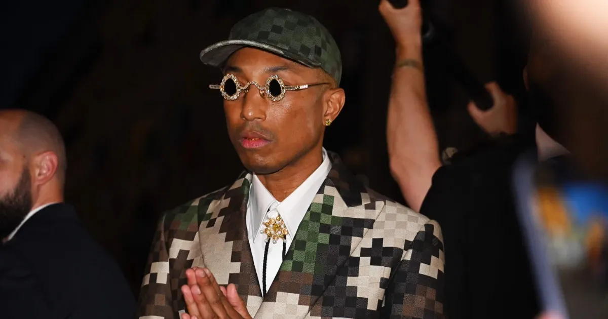 A black man singer producer and desginer named Pharrell Williams wearing his creations for Louis Vuitton including a green pixelated cap and a green white blazer.
