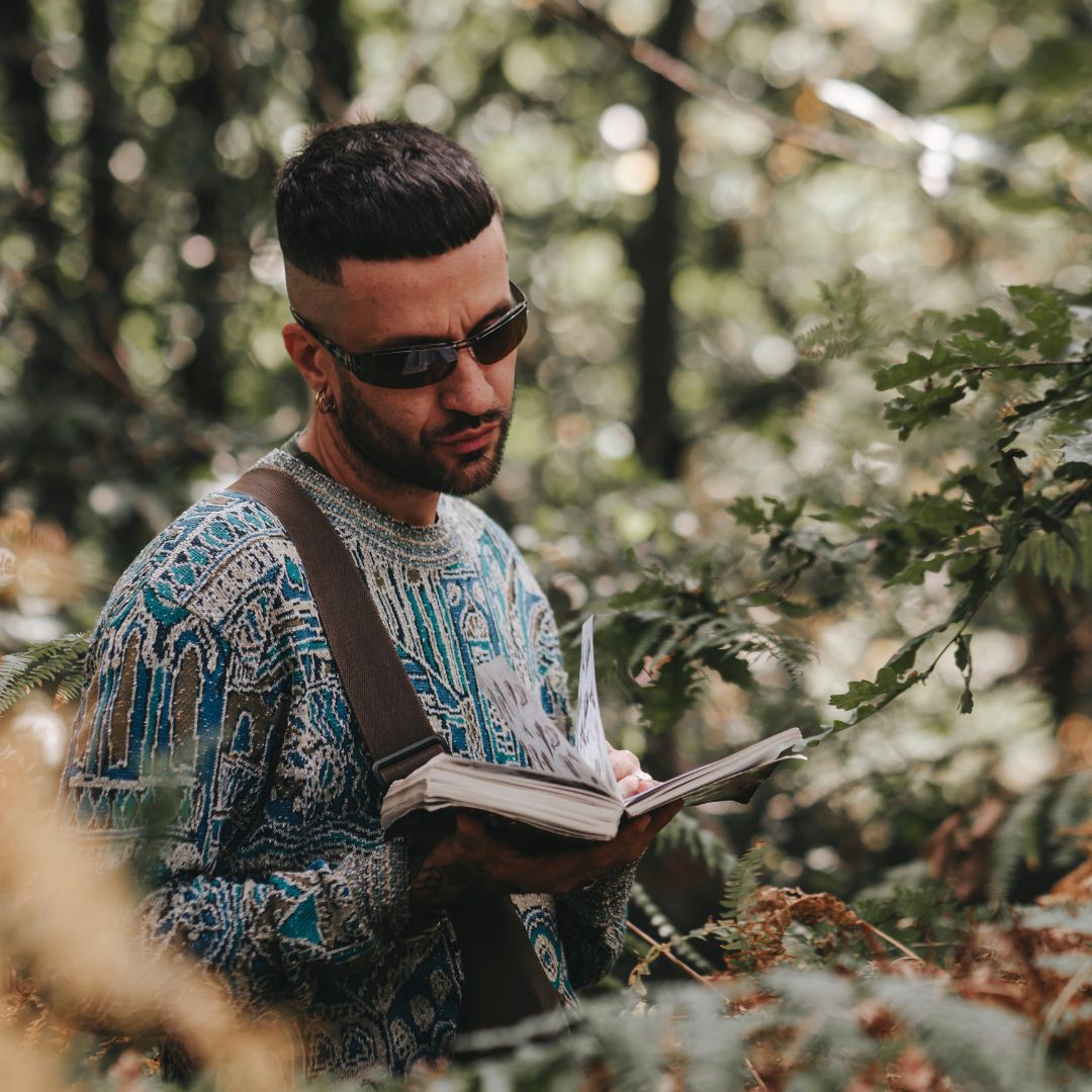 Rapper Pepe Nocciola in the ferns reading a book about wildlife